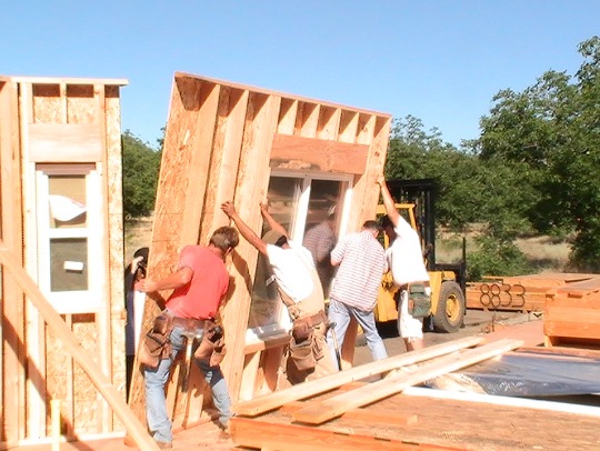 Wall panels with the window installed is lifted into place by crew